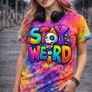 May include: A tie-dye t-shirt with the words "STAY WEIRD" in a colorful, cartoonish font. The shirt features a skull graphic and is predominantly rainbow-colored with shades of purple, orange, and blue.
