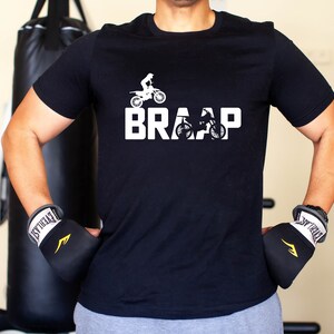 Op de afbeelding: Een zwart T-shirt met een witte afbeelding van een motorcrosser en het woord "BRRAP".