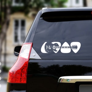 May include: A black car with a white guitar and guitar picks sticker on the back window. The sticker is in the shape of guitar picks and features a silhouette of a guitar.