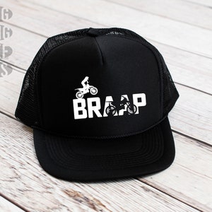 Op de afbeelding: Zwarte truckercap met een wit mesh achterpaneel. De voorkant van de cap heeft een witte afbeelding van een crossmotor en het woord "BRAAP".