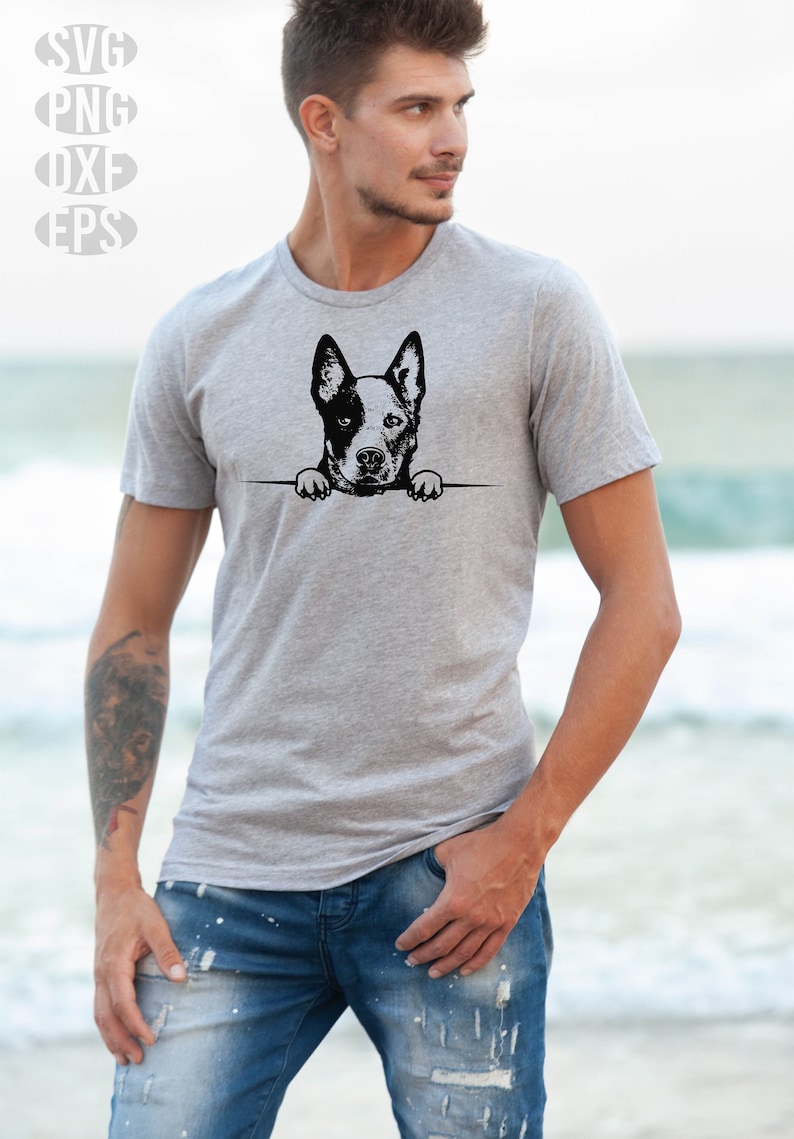 May include: A gray t-shirt featuring a black and white graphic of a dog's head and paws peeking over a horizontal line. The image includes the text "SVG, PNG, DXF, EPS" in the upper left corner. The person is wearing blue jeans.