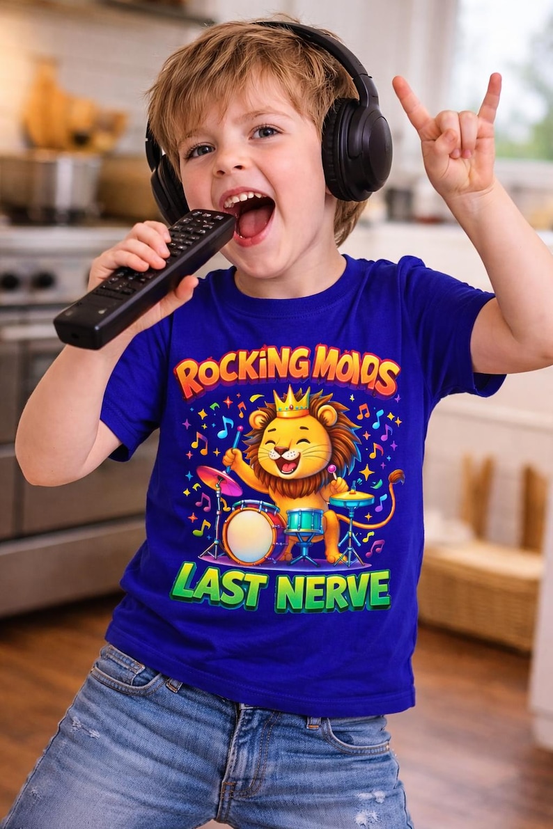May include: A young child wearing headphones and a blue t-shirt with the text "Rocking Mods" and "Last Nerve". The shirt features a cartoon lion playing drums. The child is holding a remote control and making a rock and roll hand gesture.