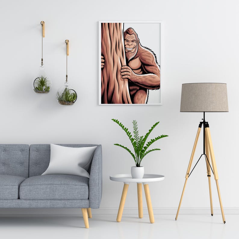Puede incluir: Ilustraci&oacute;n enmarcada de un Bigfoot sonriente asom&aacute;ndose detr&aacute;s de un &aacute;rbol. La obra de arte presenta sombreado detallado y una paleta de colores marrones y beiges. La imagen se muestra en una pared blanca sobre un sof&aacute; gris.