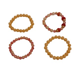 May include: Four beaded bracelets in shades of orange, pink, and red. The bracelets are made of small, round beads strung together. The beads have a glossy finish, and the bracelets are arranged in a square formation.