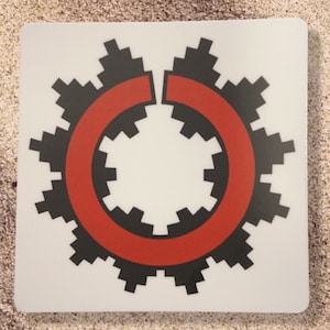May include: A white sticker with a black and red geometric design. The design is a circle with a red ring around it. The circle is made up of black squares.