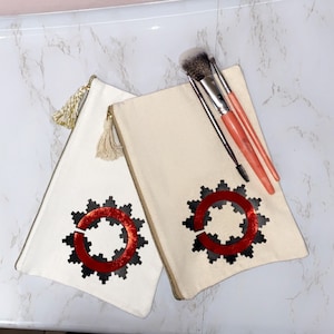 May include: Two white canvas makeup bags with red and black geometric designs. The bag on the right has three makeup brushes inside.