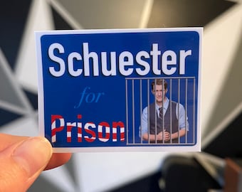 May include: A blue and white sticker with the text "Schuester for Prison" and a photo of a man in a white shirt and waistcoat looking through a jail cell window.