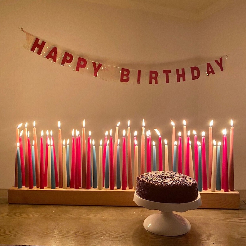 Op de afbeelding: Een chocoladetaart met kaarsen op een houten basis. De kaarsen zijn aangestoken en er hangt een banner met de tekst "Happy Birthday" boven de taart.