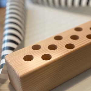 Op de afbeelding: Een natuurlijke houten potloodhouder met meerdere ronde gaten om potloden of andere schrijfbenodigdheden in op te bergen. De houder is gemaakt van licht hout met een gladde afwerking.
