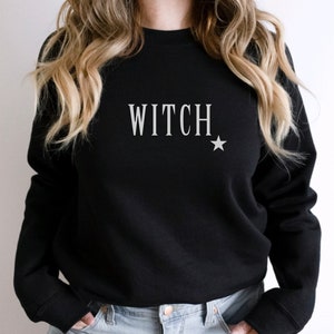 Puede incluir: Sudadera negra con la palabra "WITCH" en letras blancas y una pequeña estrella blanca.