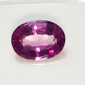May include: A vibrant purple oval-shaped gemstone with a smooth, polished surface.