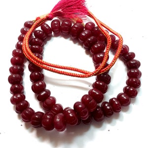 May include: A red gemstone mala necklace with a red tassel. The beads are round and have a slightly textured surface.