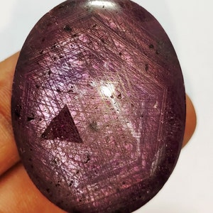 Könnte beinhalten: Ein großer, ovaler, violetter Edelstein mit einem sternförmigen Muster und einer dreieckigen Form in der Mitte.