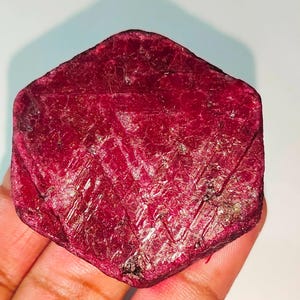 Puede incluir: Una gran gema de rubí rojo intenso con forma hexagonal y una superficie rugosa y facetada.