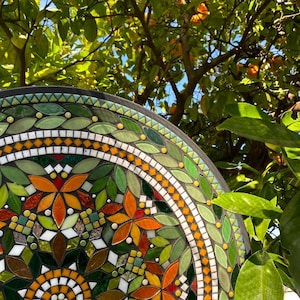 Peut inclure: Une œuvre d'art murale en mosaïque circulaire présentant un motif complexe de carreaux de verre dans des tons de vert, orange, jaune et blanc. Le design comprend un motif floral central entouré d'anneaux concentriques de carreaux en forme de feuille.