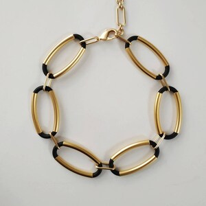 Puede incluir: Un brazalete de eslabones ovalados en oro y negro con cierre de cadena dorada.