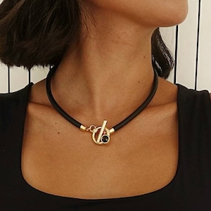 May include: A black choker necklace with a gold toggle clasp and a black gemstone.
