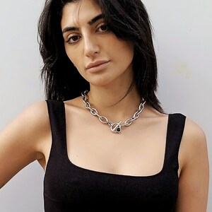 May include: A woman wearing a black tank top with a silver chain necklace featuring a black stone accent.