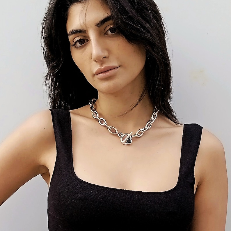 May include: A woman wearing a black tank top with a silver chain necklace featuring a black stone accent.