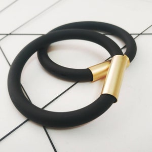 May include: Two black silicone bracelets with a gold metal accent. The bracelets are stacked on top of each other.