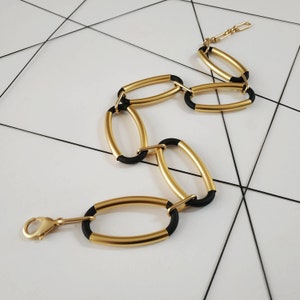 Puede incluir: Un collar de cadena de oro con eslabones ovalados negros. La cadena tiene un cierre de mosquet&oacute;n.