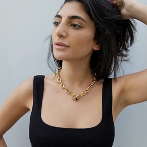 May include: A gold chain necklace with a large, chunky link design. The necklace has a toggle clasp with a black stone accent.