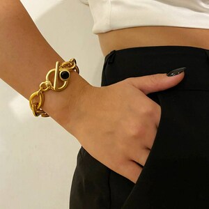 May include: A gold chain bracelet with a large, black stone toggle clasp.