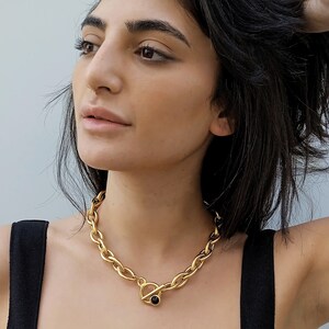 May include: A gold chain necklace with a large, chunky link design. The necklace has a toggle clasp with a black stone accent.