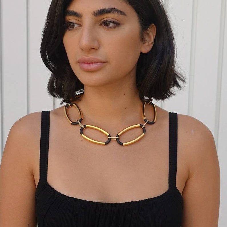 Puede incluir: Un collar de cadena dorado y negro con eslabones ovalados. El collar lo lleva una persona con el pelo oscuro.