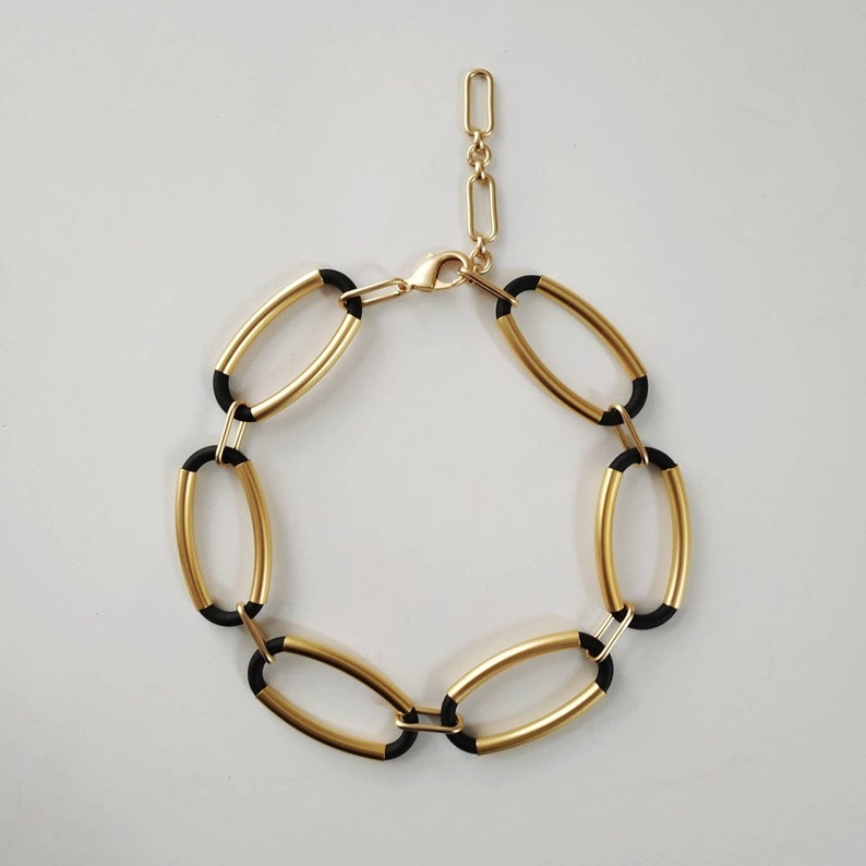 Puede incluir: Un brazalete de eslabones ovalados en oro y negro con cierre de cadena dorada.