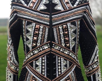 Könnte beinhalten: Eine schwarze Showjacke mit geometrischem Design mit weißen, silbernen und kupferfarbenen Akzenten. Die Jacke hat einen Reißverschluss und lange Ärmel.