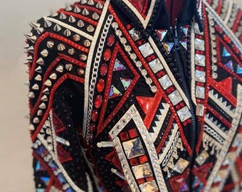 Könnte beinhalten: Eine schwarze Showjacke mit roten und weißen geometrischen Mustern und Strasssteinen. Die Jacke hat einen Reißverschluss und einen Stehkragen. Die Schultern sind mit silbernen Nieten verziert.