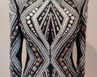 May include: A black show jacket with a silver and white geometric design. The jacket is embellished with rhinestones and beads. The text "Alina by Alina" is printed on the bottom of the jacket.