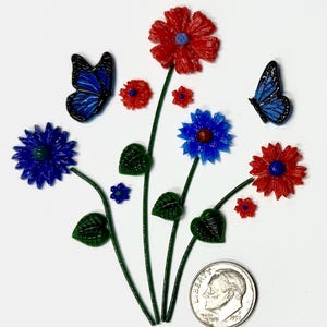 Op de afbeelding: Een verzameling miniatuur bloem- en vlinderversieringen met rode en blauwe bloemen, groene stelen en bladeren, vergezeld door twee blauwe vlinders. Een Amerikaanse dubbeltje is onderaan geplaatst als schaalreferentie.