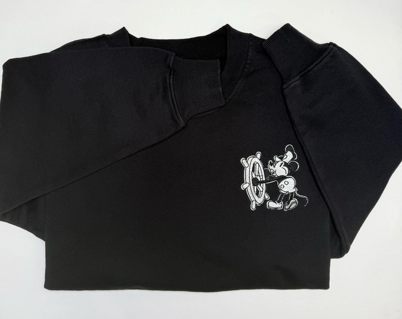May include: Black sweatshirt with a white embroidered image of Mickey Mouse holding a ship's wheel.