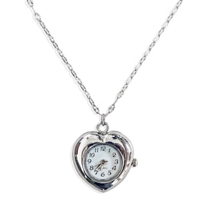 May include: A silver heart-shaped pendant necklace with a small watch face inside. The watch face has black hands and black numbers on a white background. The necklace has a silver chain.
