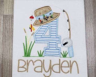 May include: A white t-shirt with a blue and white striped number four, a brown fishing hat, a fishing rod, and green grass. The name "Brayden" is embroidered in brown below the number.