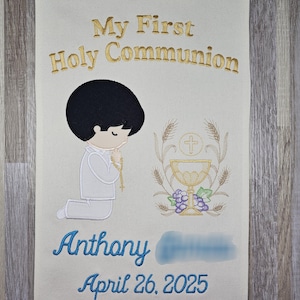 May include: A white banner with gold embroidery that says "My First Holy Communion". A cartoon boy is kneeling in prayer with a chalice and grapes in the background. The banner also says "Anthony" and "April 26, 2025".