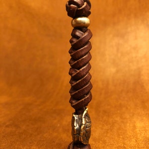May include: A brown leather cord with a gold bead and a brass turtle charm. The cord is braided and knotted.