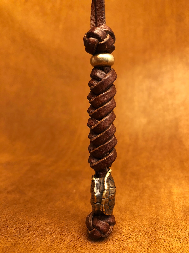May include: A brown leather cord with a gold bead and a brass turtle charm. The cord is braided and knotted.