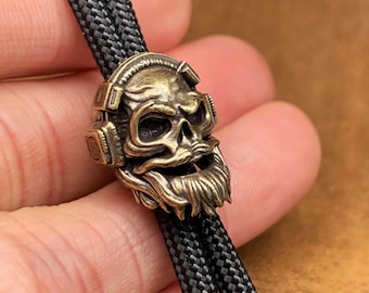 Cuenta de latón con forma de calavera y cuchillo: dije para cordón de músico, pátina oxidada estilo latón, el color cambia de amarillo brillante a cobre antiguo cálido.
