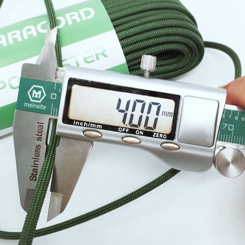 May include: A coil of olive green paracord with a white paper label reading PARACORD and POLYESTER. A stainless steel digital caliper is measuring the diameter of the cord, showing a clear reading of 4.00 mm on the digital display screen.
