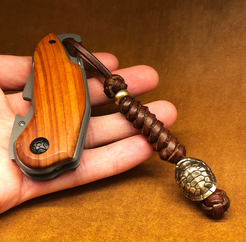 May include: A small, wooden-handled pocket knife with a bottle opener and a leather lanyard with a brass bead and a decorative brass charm.