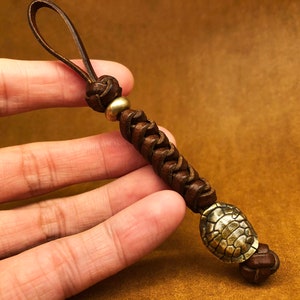 May include: A brown leather key chain with a braided design and a brass turtle charm.