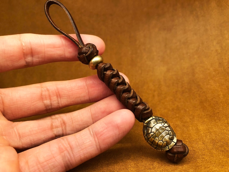 May include: A brown leather key chain with a braided design and a brass turtle charm.