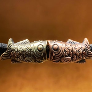 以下が含まれることがあります： 鱗と目が詳細に描かれた金色の魚の形をしたトグル留め具が2つ。留め具は互いに接続されており、金属製です。