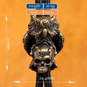 Puede incluir: Colgante de b&uacute;ho de color bronce con base de calavera, sujeto a un cord&oacute;n negro. El colgante mide 30 mm de largo y 19,4 mm de ancho. El agujero es de 6 mm y el peso es de 16,6 g. El b&uacute;ho tiene detalles de plumas y ojos.