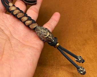 May include: A black and brown paracord keychain with a brass lion head charm and two black cord ends with brass accents.