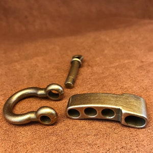 Peut inclure: Trois pièces de quincaillerie en laiton, dont un anneau en D, une pièce rectangulaire à cinq trous et une pièce à visser.
