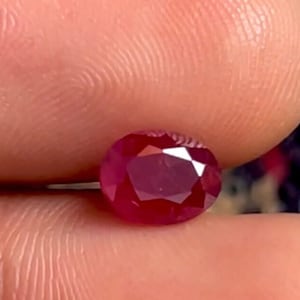 May include: A deep red oval-shaped ruby gemstone.